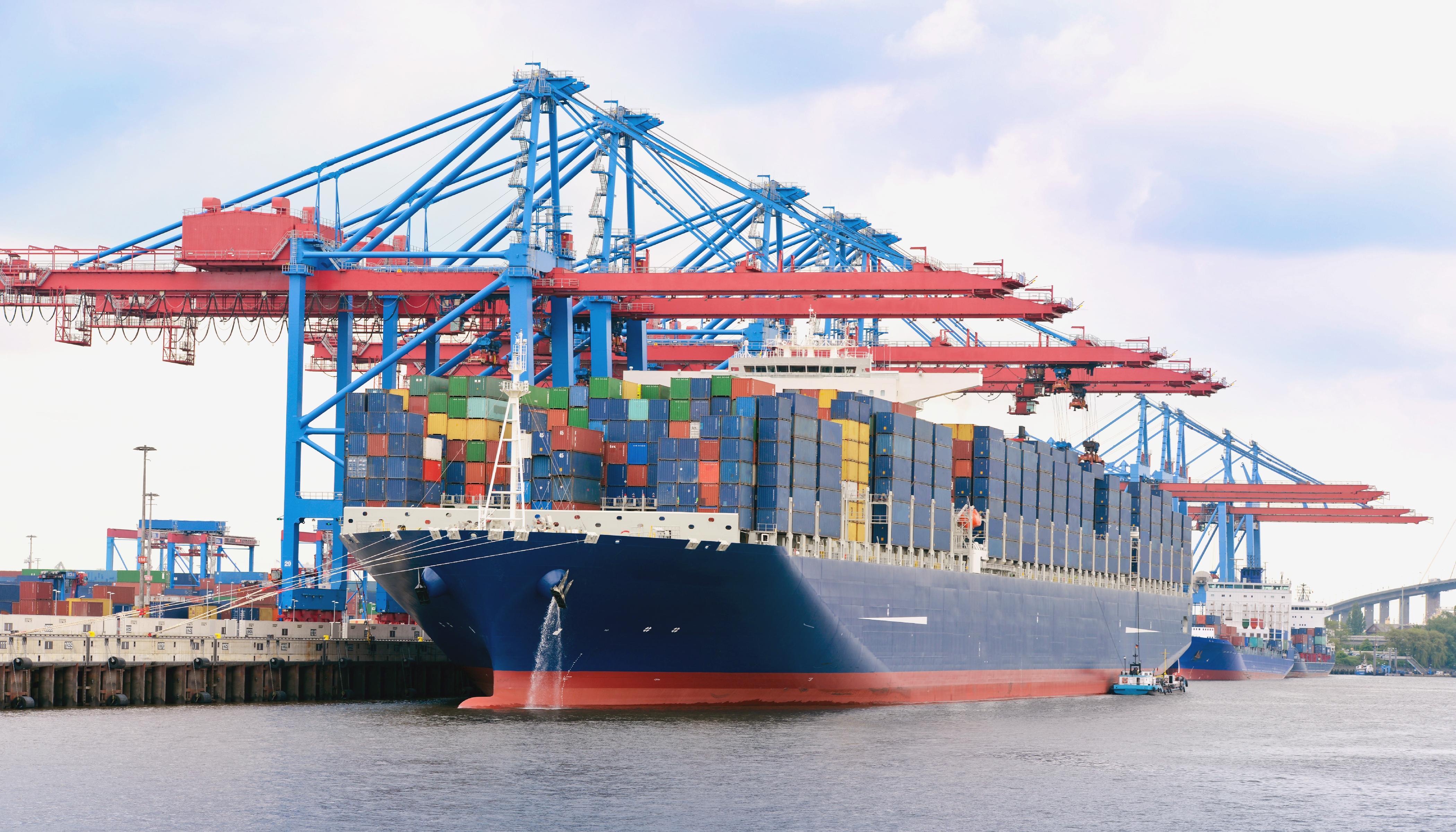 A fully loaded container ship in a harbor. Above the boat you can see various cranes for loading the ship. Source: Stefan Körber/stock.adobe.com A fully loaded container ship in a harbor. Above the boat you can see various cranes for loading the ship. Source: Stefan Körber/stock.adobe.com